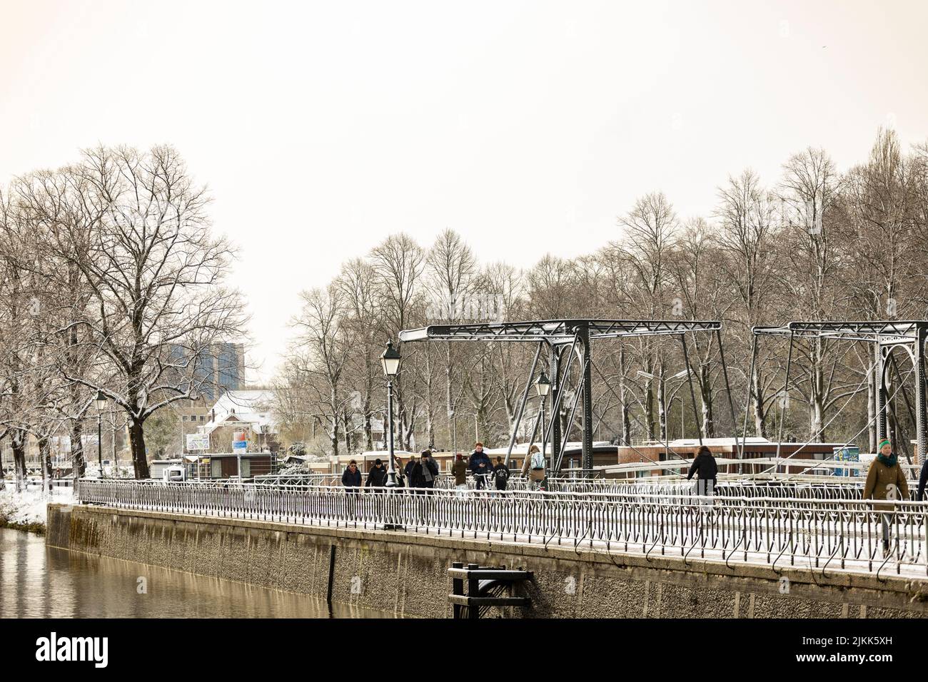 Scena di strada con persone che camminano lungo il canale Leidsche Rijn chiusa-cancello boulevard a Utrecht con ponte di acciaio sullo sfondo in inverno Foto Stock