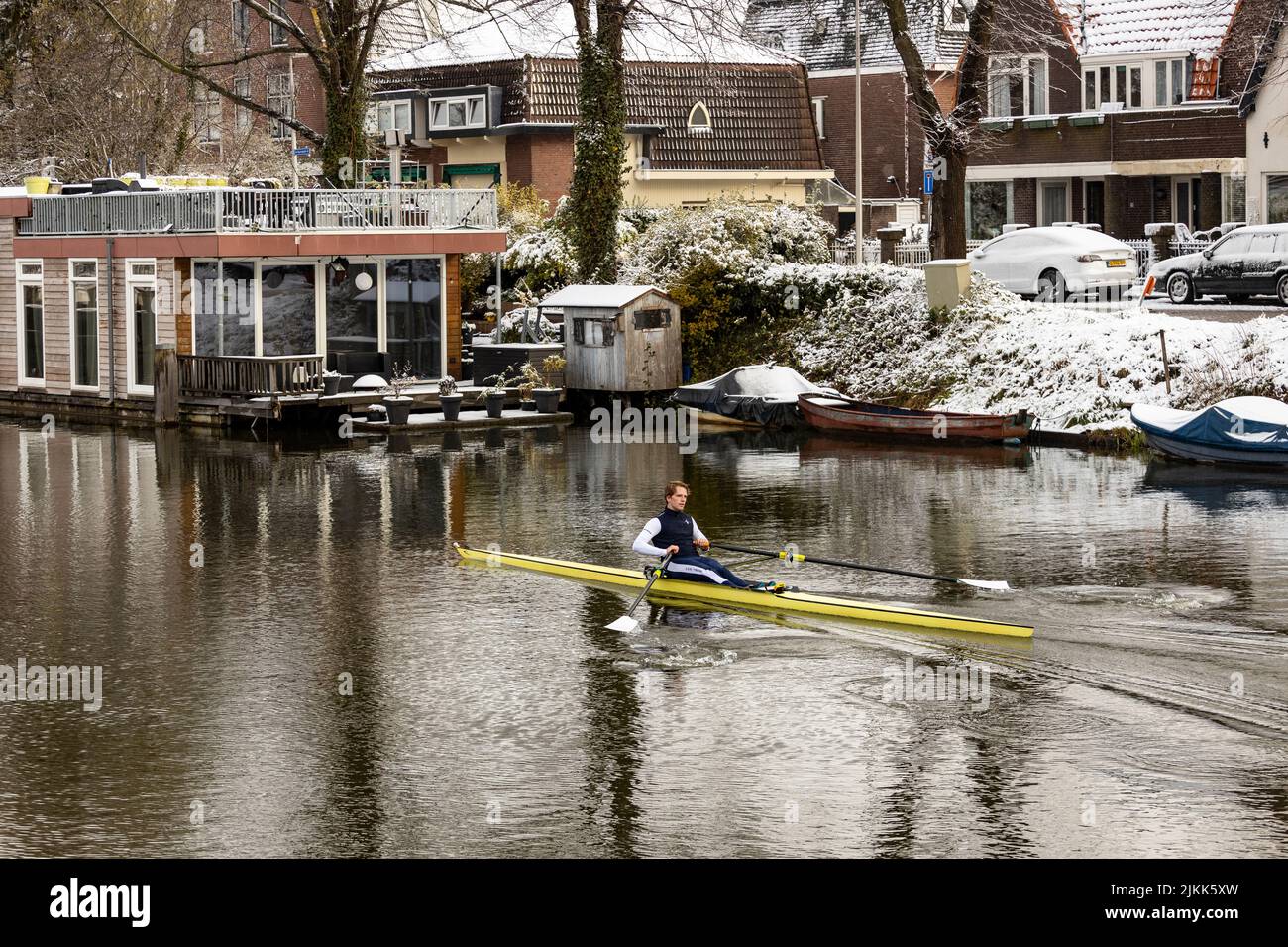Sport di canottaggio con una persona che scivola attraverso il canale con la neve sullo sfondo passando case galleggianti Foto Stock