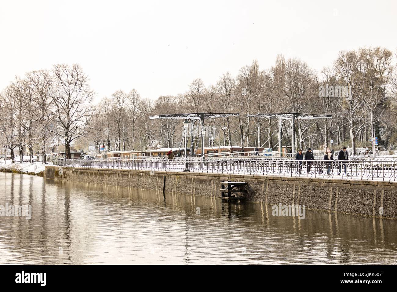 Le persone che camminano lungo il canale Leidsche Rijn sluice-gate boulevard con ponte di acciaio sullo sfondo nella stagione invernale neve scena. Foto Stock