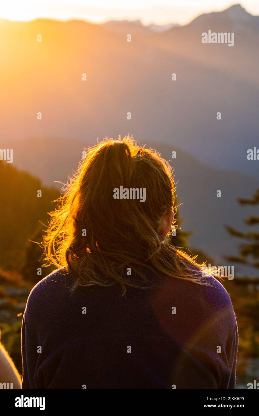 Una vista posteriore di una donna che guarda le montagne con i raggi del sole Foto Stock