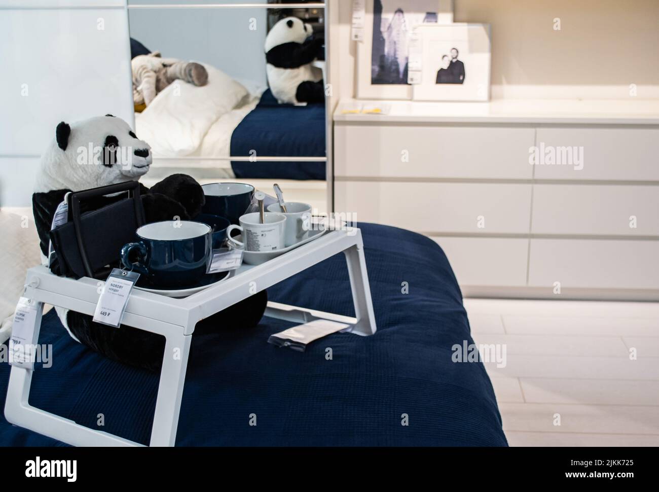 Mosca, Russia, Settembre 2019:IKEA showroom: la camera da letto è bianca con accenti blu. Panda seduta sul letto ad un tavolo portatile con tazze e ciotole, el Foto Stock