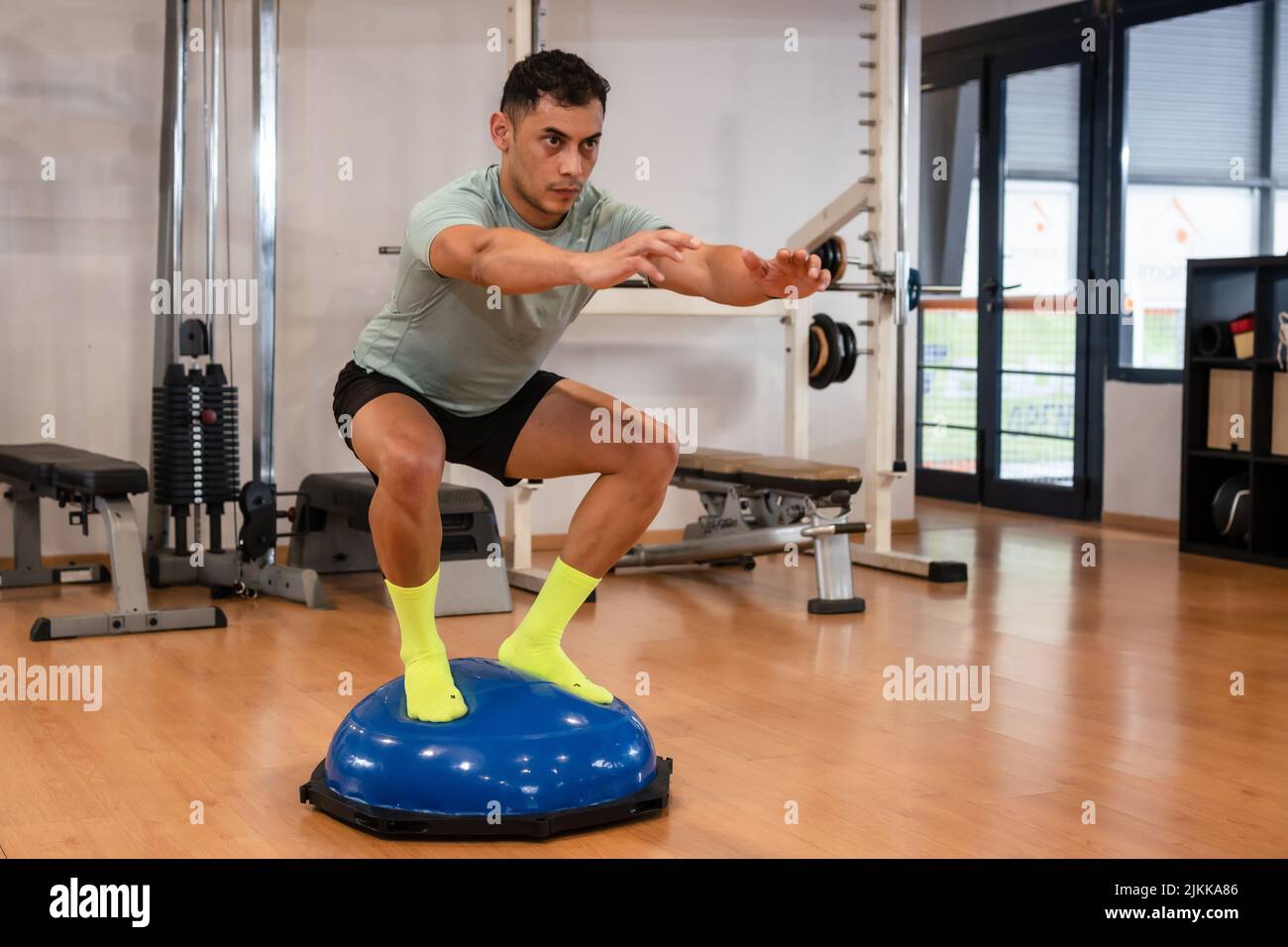 Ritratto di un uomo caucasico in palestra facendo esercizi di equilibrio per la caviglia su una sfera di gomma, vita sana e sana facendo sport Foto Stock