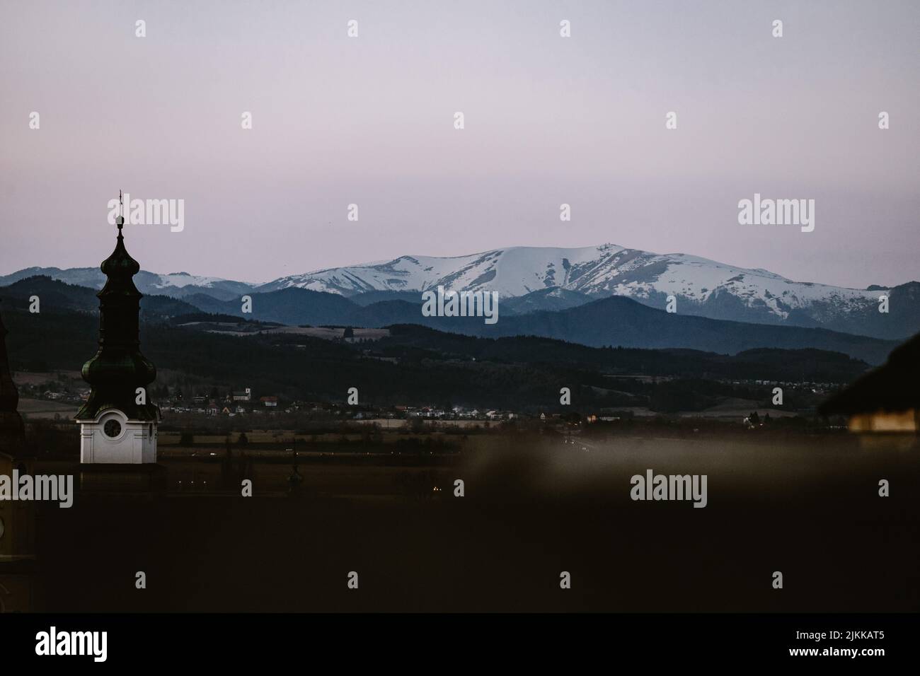 Una chiesa con la cima parzialmente innevata di Krizna sullo sfondo della città di Zvolen durante l'ora blu Foto Stock