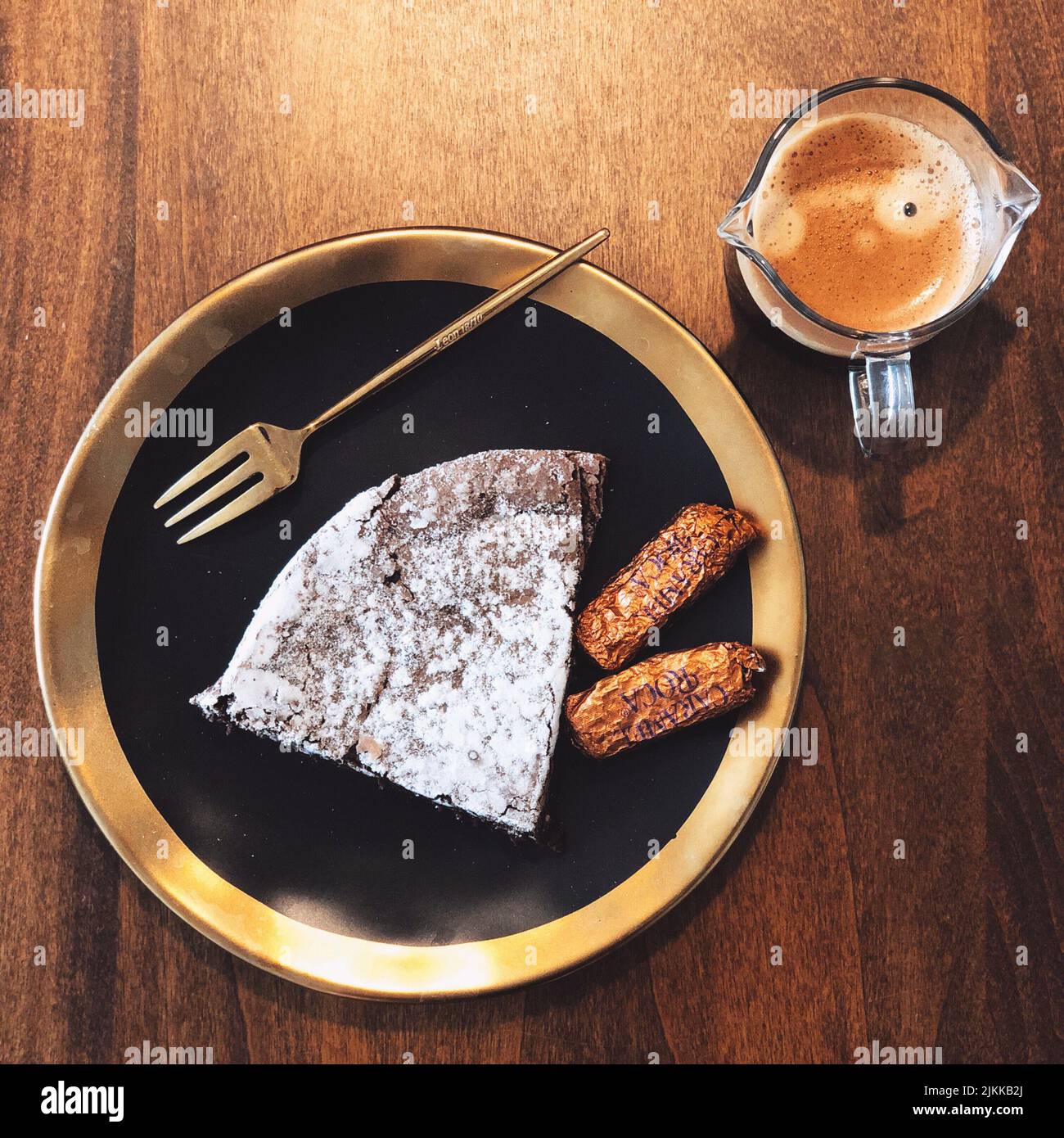 Vista dall'alto di un pezzo di torta e due biscotti sul piatto nero e dorato con una tazza di caffè Foto Stock