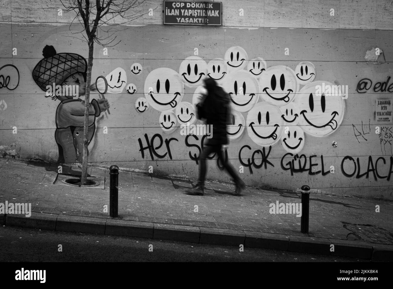 Una scala di grigi di un uomo che passa per una strada a Istanbul accanto a un muro ha arte graffiti di strada Foto Stock