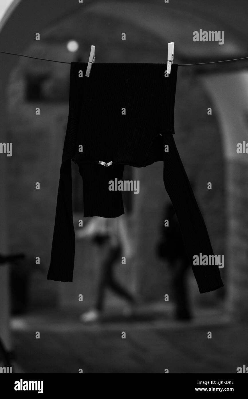 Immagine verticale di un maglione nero appeso a un filo su uno sfondo sfocato in scala di grigi Foto Stock