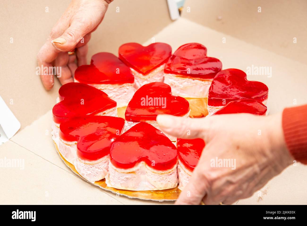 Una romantica torta a forma di cuore rosso è tenuta dalle mani delle donne Foto Stock