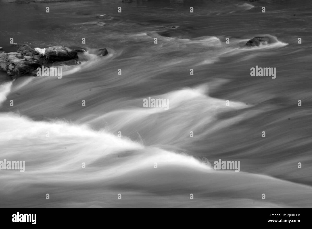 Una scala di grigi di onde di fiume con pietre Foto Stock