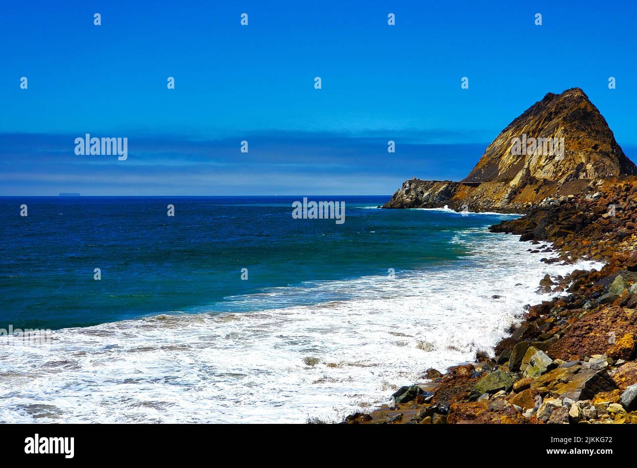 Una vista panoramica dell'oceano dalla riva - spiaggia rocciosa, onde, scogliera e cielo blu Foto Stock
