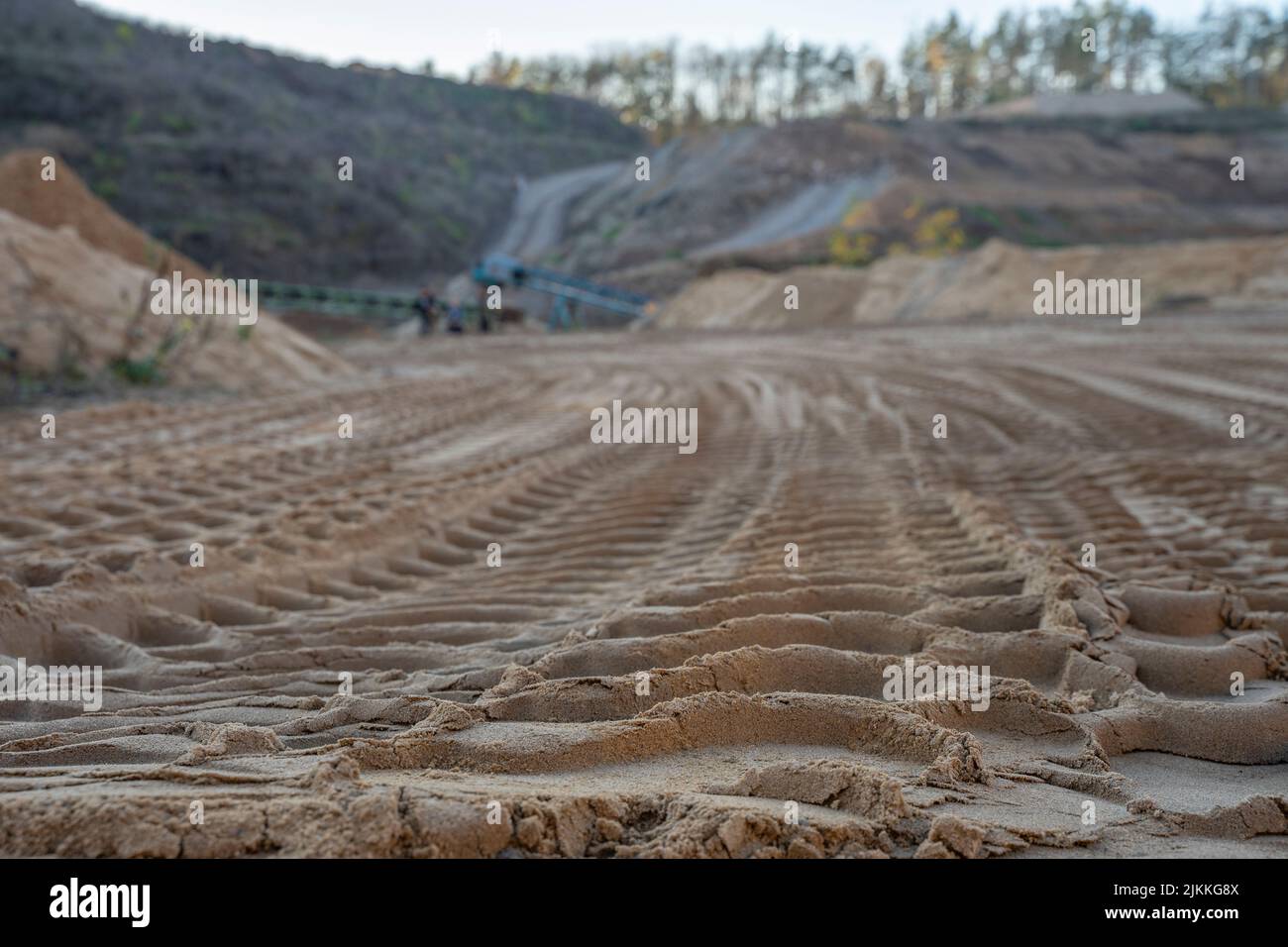 Un'immagine poco profonda di un'area di sabbia con segni di pneumatici e processi industriali in background Foto Stock