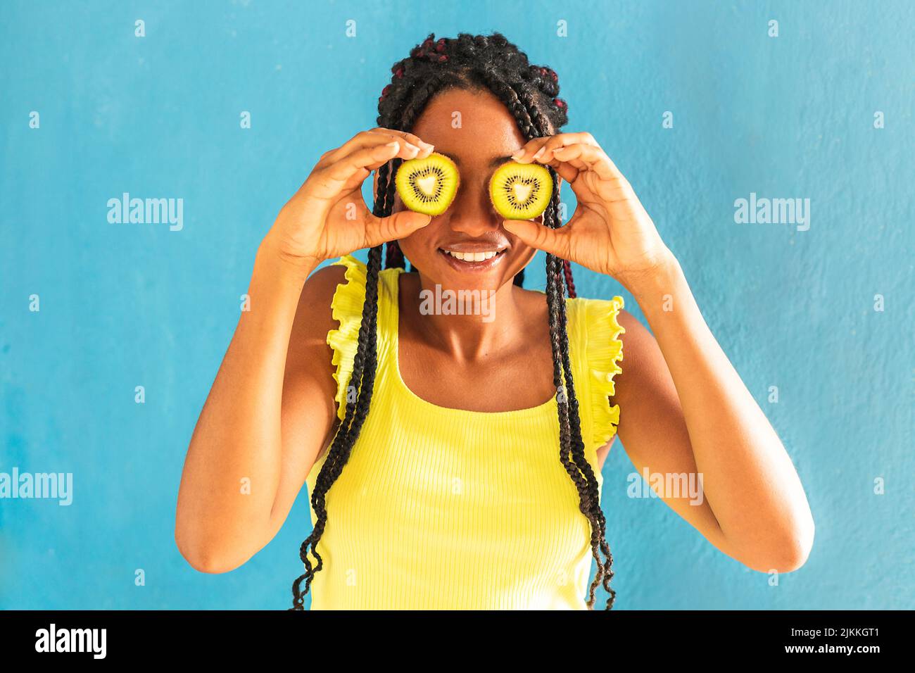 Una giovane ragazza allegra di razza mista che tiene kiwi davanti ai suoi occhi Foto Stock