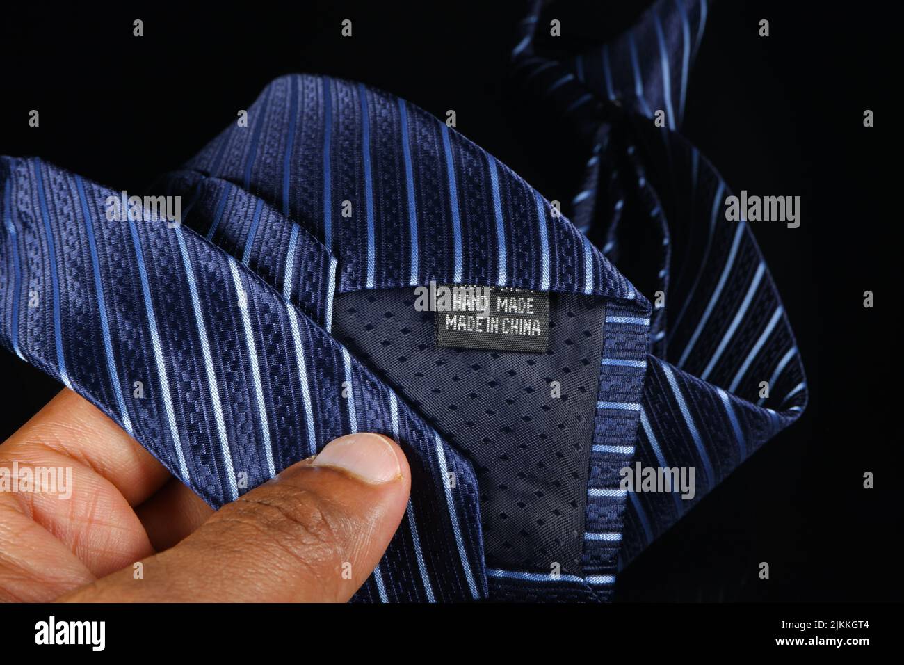 Una mano dell'uomo che tiene una cravatta blu a strisce con un'etichetta "fatta a mano in Cina" Foto Stock