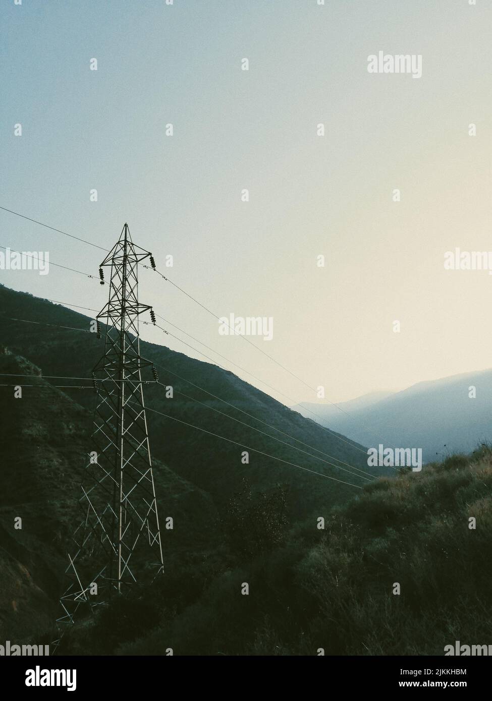 Uno scatto verticale delle linee di trasmissione dell'elettricità contro montagne e cielo Foto Stock