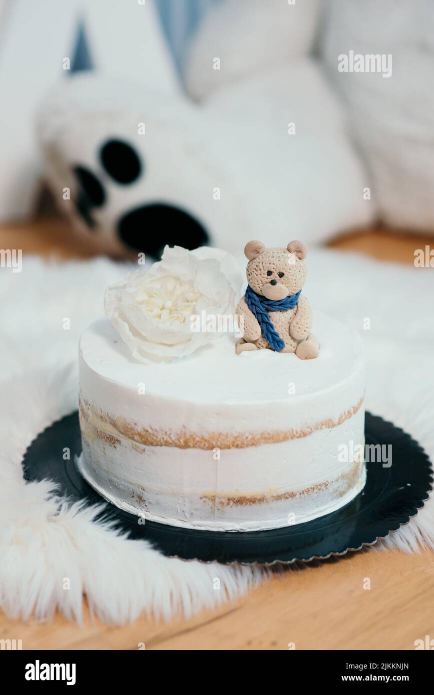 Un colpo verticale di una torta bianca con un fiore e un orso marrone su di essa, isolato su uno sfondo sfocato Foto Stock