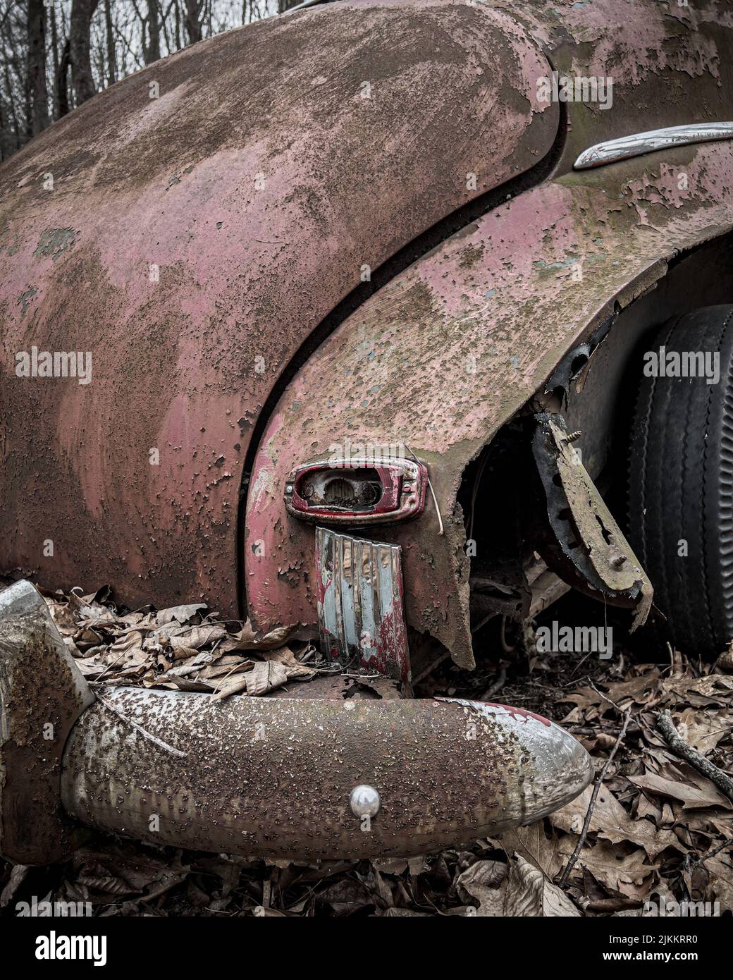 Un colpo verticale di parti di una vecchia auto abbandonata rotta in una foresta Foto Stock