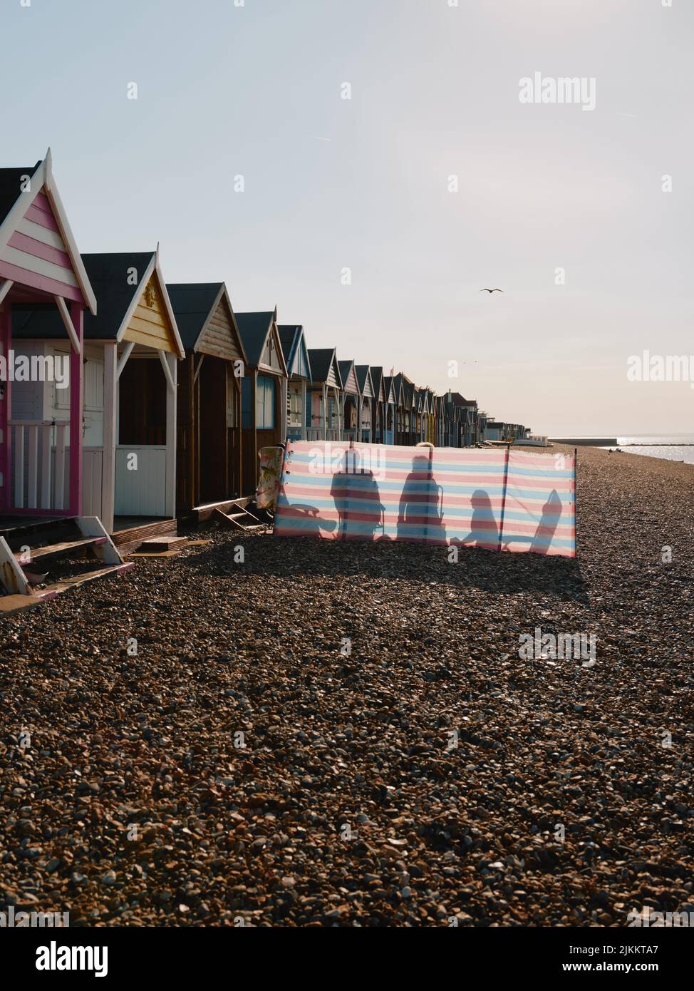 La spiaggia estiva, le capanne da spiaggia, il windbreaker e la famiglia si godono una giornata estiva sulla spiaggia di ghiaia Herne Bay North Kent Coast Inghilterra UK Foto Stock