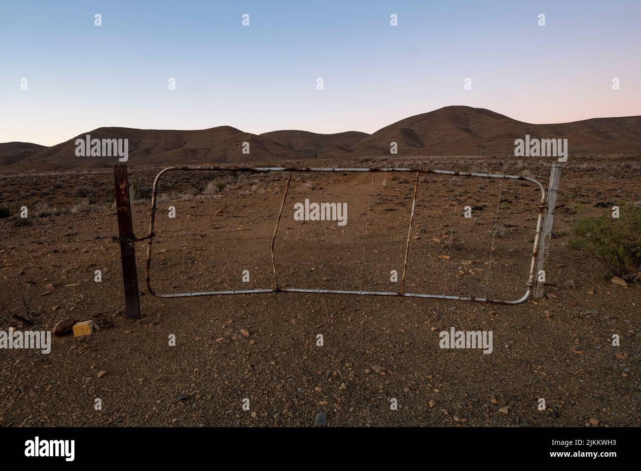 Una vista panoramica di un cancello metallico abbandonato nel Capo Occidentale di Karoo, Sud Africa su un campo asciutto al tramonto Foto Stock