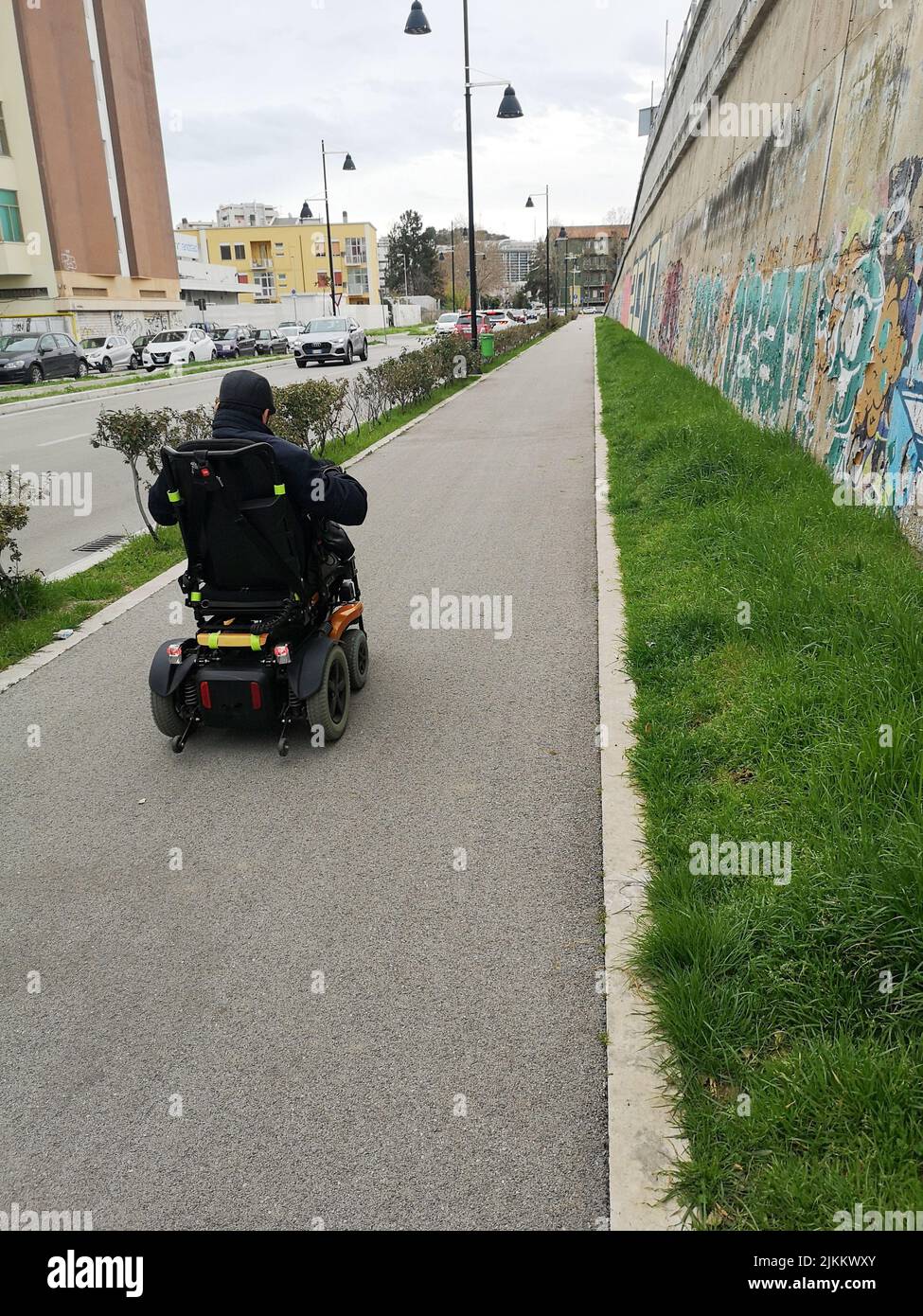 Un'immagine verticale di un uomo in sedia a rotelle elettrica sul marciapiede della città con graffiti Foto Stock