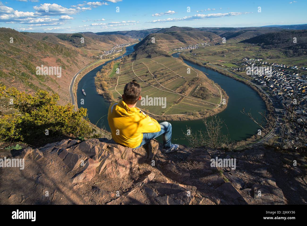 Un colpo ad angolo alto di un giovane seduto al bordo della gola godendo dell'affascinante vista del lago e delle montagne Foto Stock