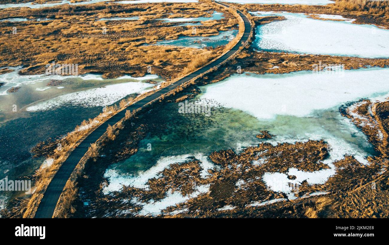 Una vista agghiacciante della neve che si scioglie su un campo e su una strada che conduce ad una città Foto Stock