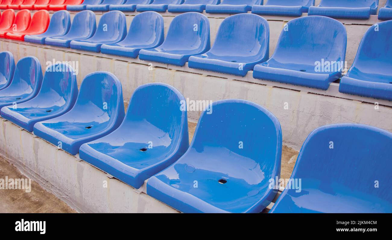 Vuoto bleacher nello stadio sportivo in tempo piovoso. Sedili colorati bagnati nello stadio di strada. Piove. Primo piano Foto Stock