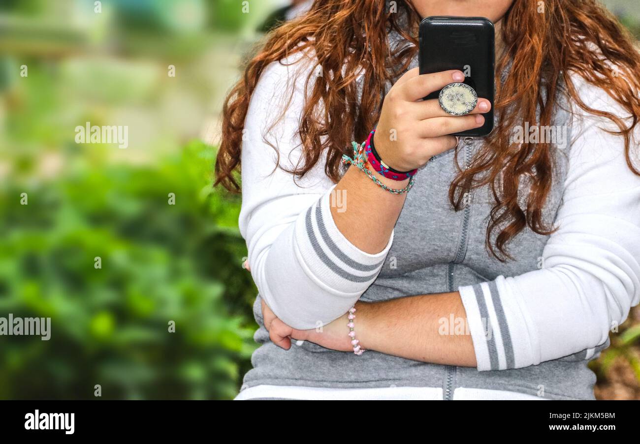 Primo piano di donna che tiene e leggere da un telefono cellulare in custodia nera con impugnatura sul retro - capelli lunghi con bracelets carino e top felpa - casua Foto Stock