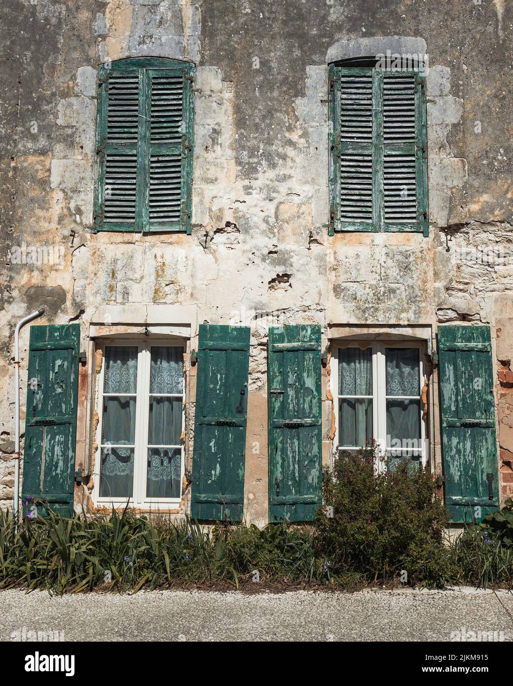 Una facciata di una casa distrutta con finestre con persiane verdi Foto Stock