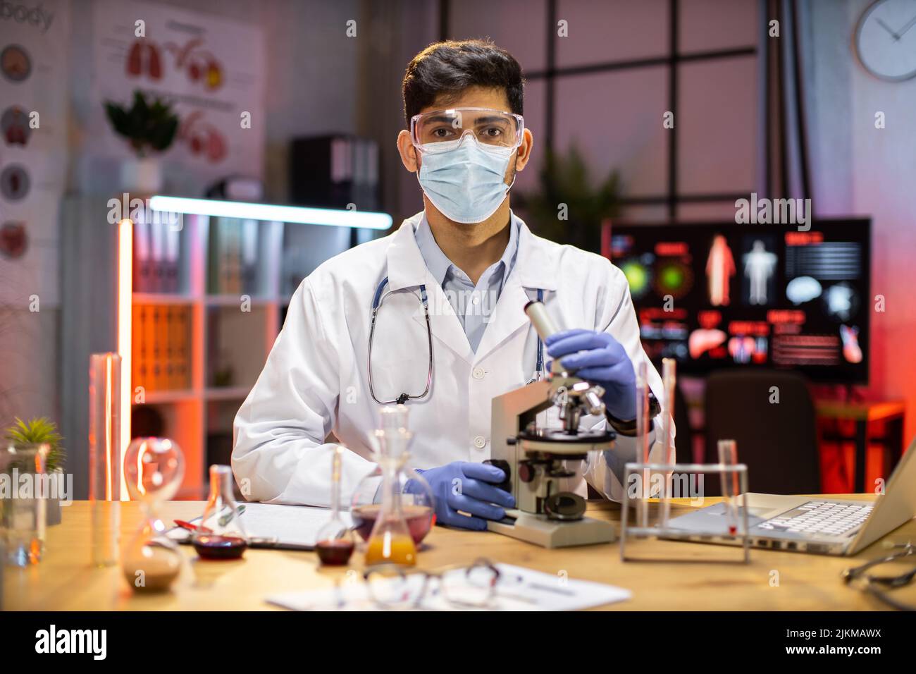 Gli scienziati o i medici maschi stanno testando i farmaci per prevenire e distruggere nuovi ceppi del virus attraverso il microscopio. Ricerca e sperimentazione di prodotti chimici efficaci. COVID-19 ora notturna. Foto Stock