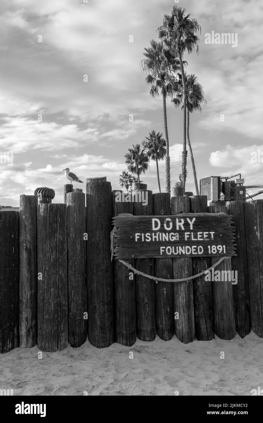 Un'immagine in scala di grigi del cartello Dory Fishing Fleet su una recinzione di legno a Newport Beach, California, USA Foto Stock