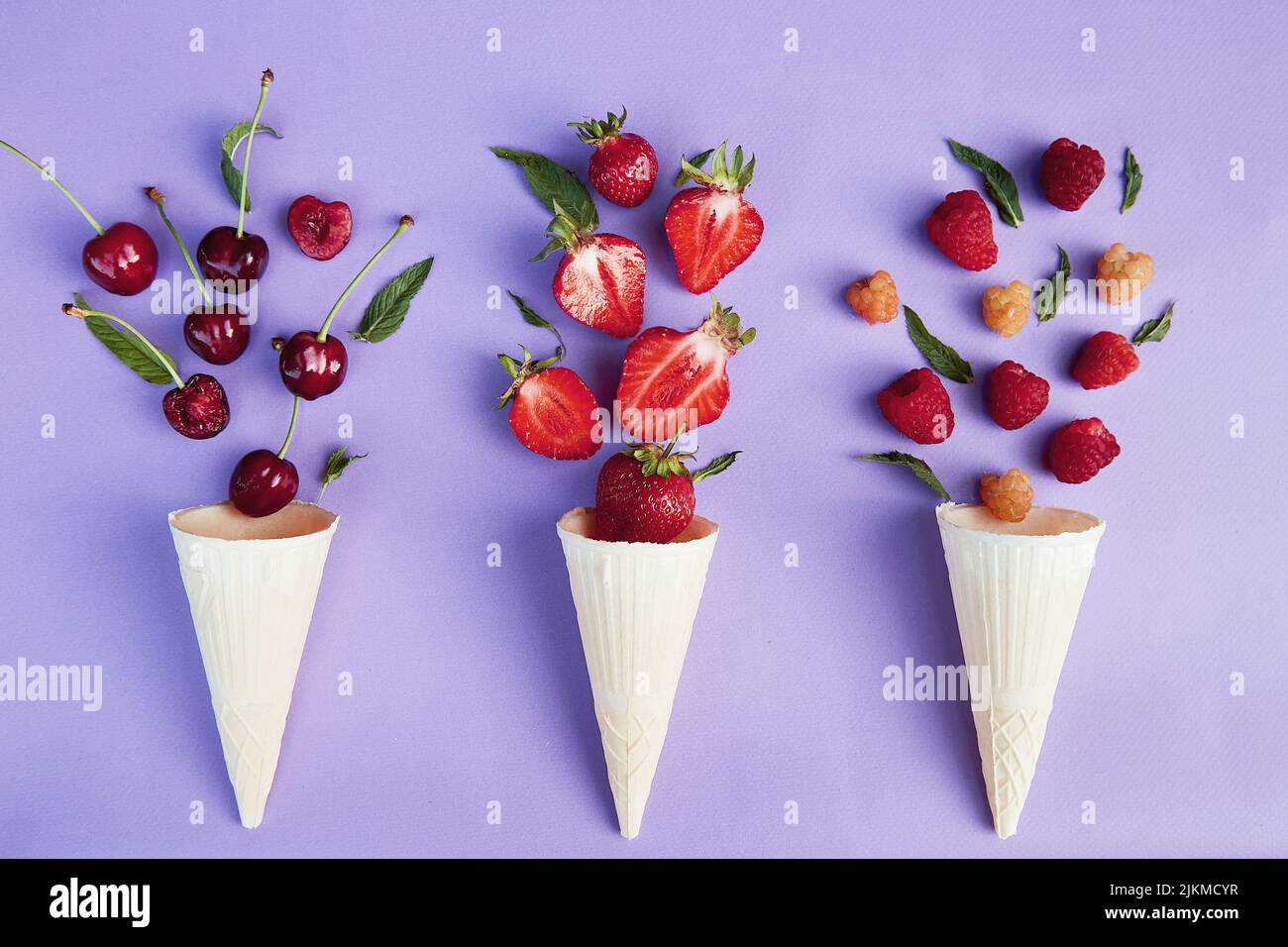 Spruzzi di bacche estive da coni gelato su sfondo viola. Estate tempo cibo piatto laici. Foto Stock