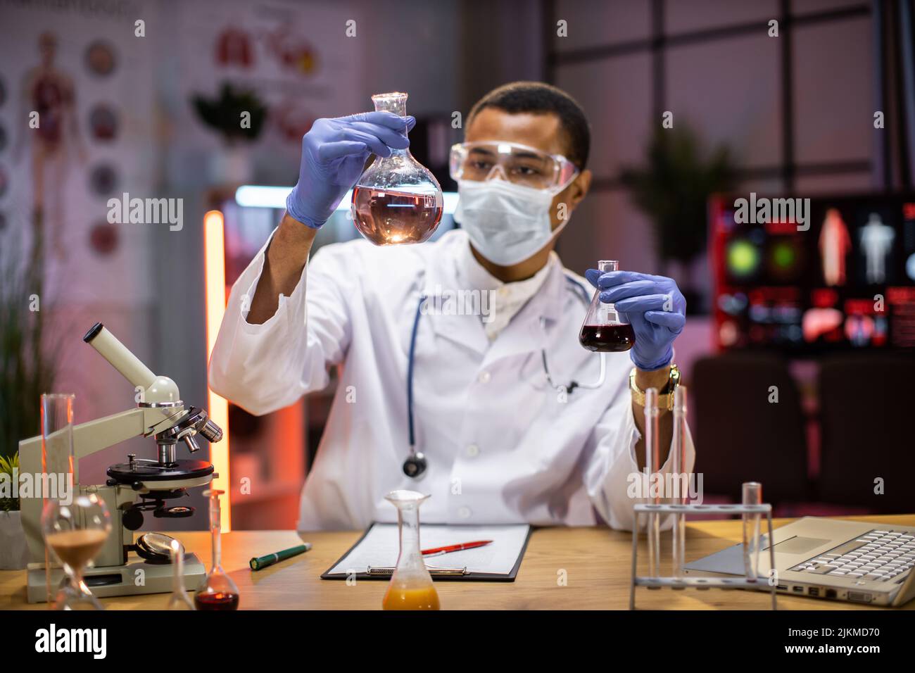 Scienziato maschile esperto in maschera protettiva e occhiali che fanno l'analisi della sostanza. Ricercatore chimico in laboratorio sterile facendo esperimenti per l'industria medica utilizzando la tecnologia moderna. Foto Stock