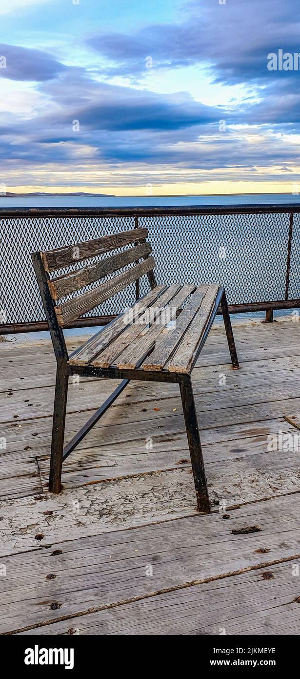 Un colpo verticale di una vecchia panca di legno vuota grunge su un terreno di legno da un cielo nuvoloso blu drammatico Foto Stock