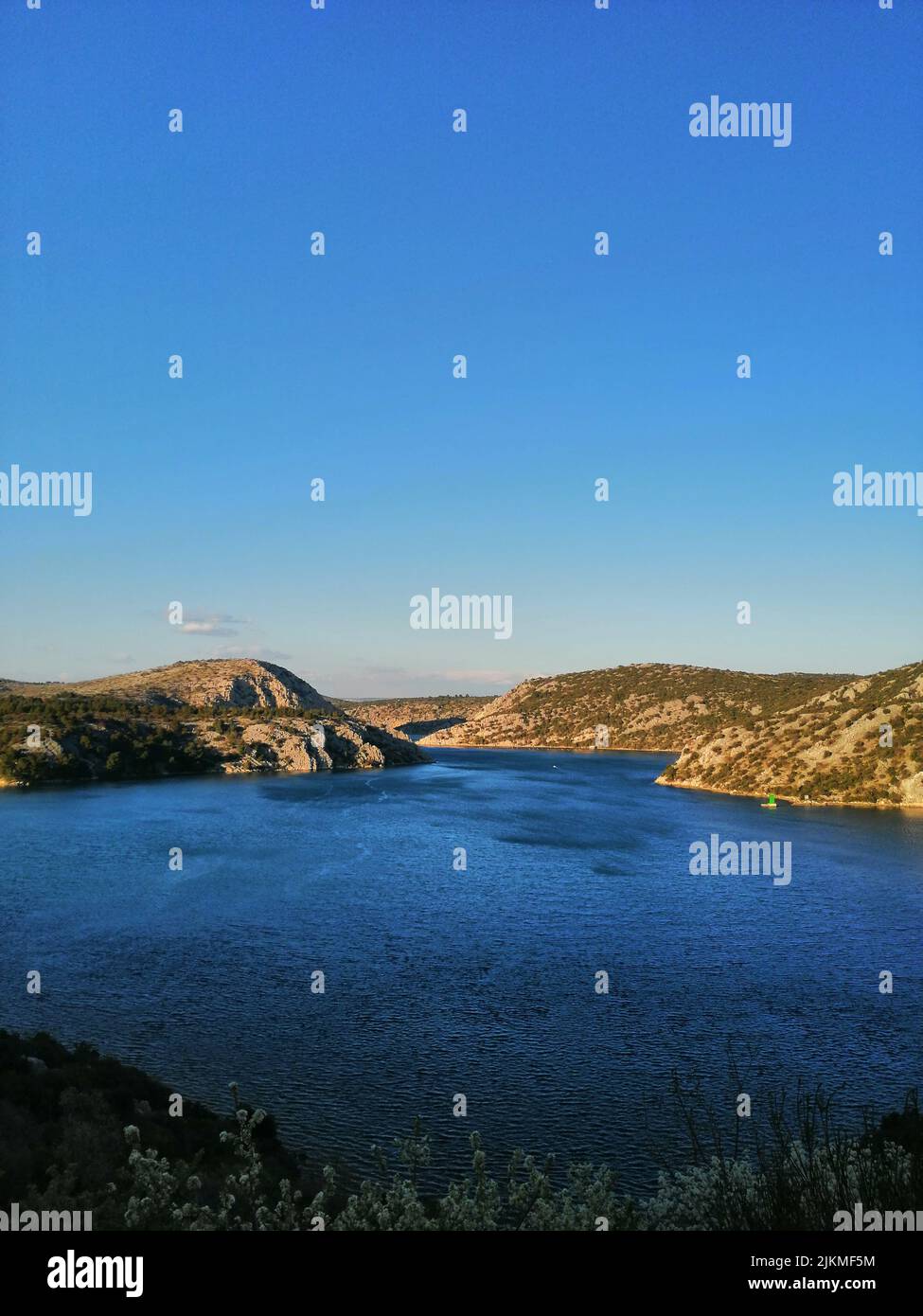 Una verticale di un lago contro le montagne coperte di alberi verdi sotto il cielo blu senza nuvole Foto Stock