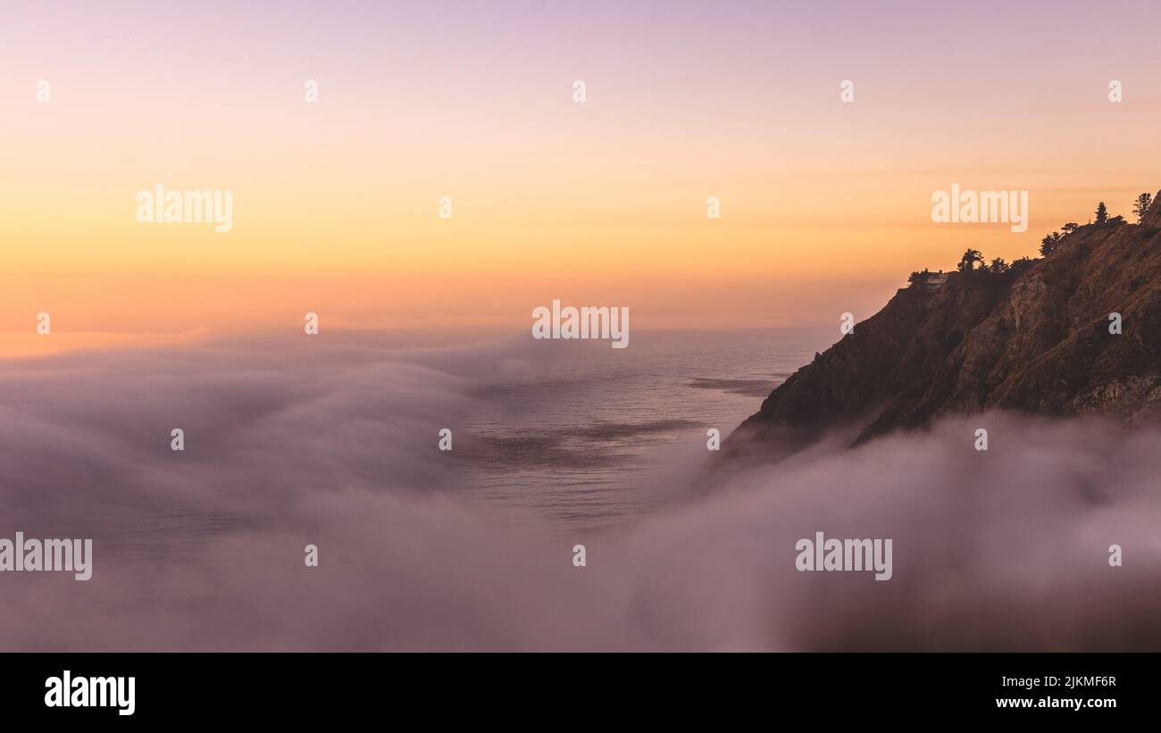 Una vista panoramica delle montagne contro il mare coperto di nebbia al mattino presto Foto Stock