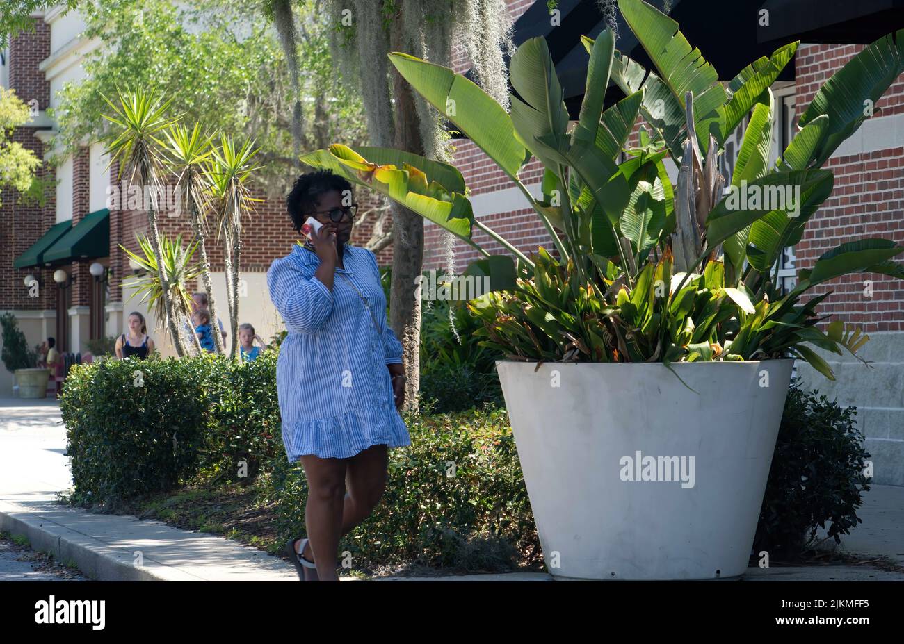 Una donna afroamericana che cammina lungo un marciapiede mentre parla al telefono nel centro di St Johns Foto Stock