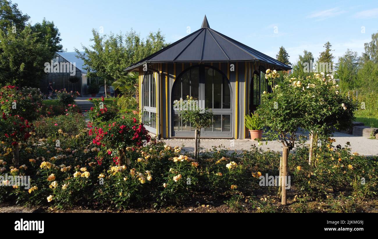 Una vista panoramica di una piccola serra circondata da alberi verdi e fiori colorati Foto Stock