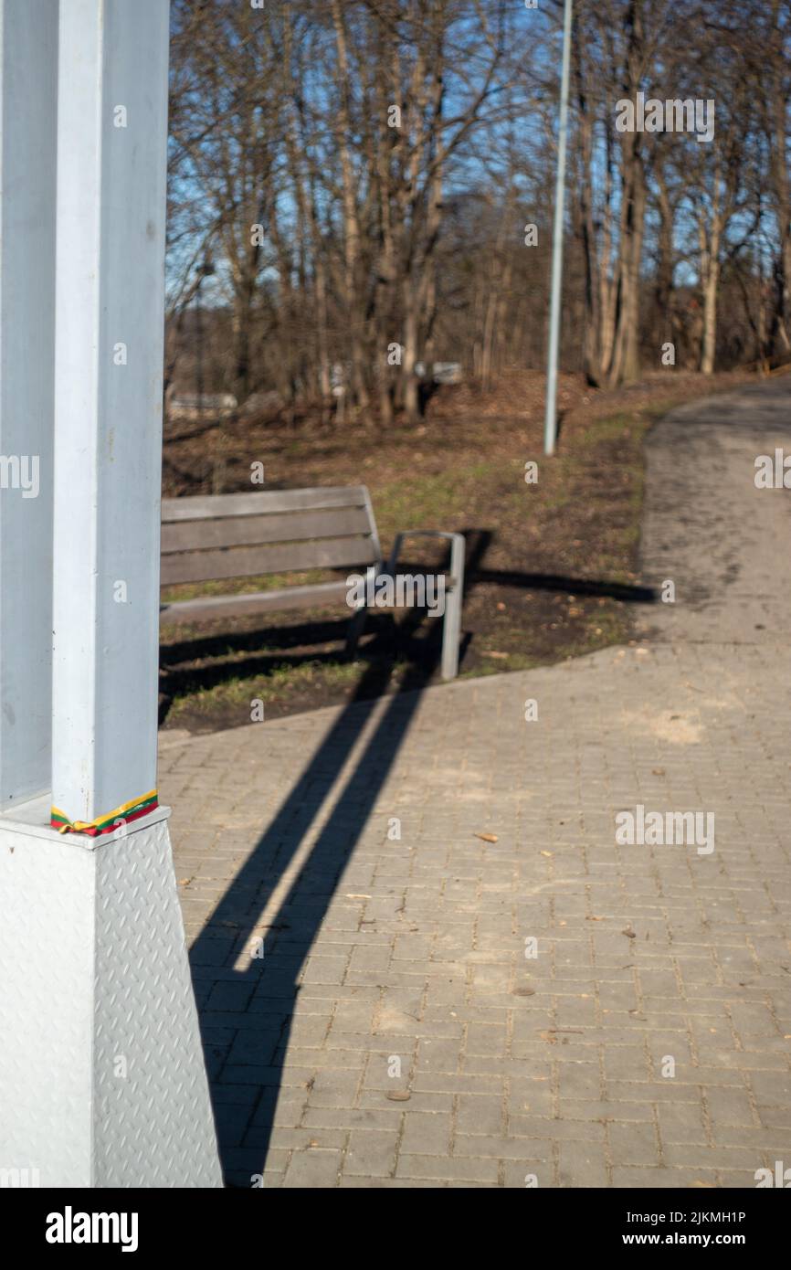 Una vista di un parco con una panca di legno vuota e alberi senza fronde in una giornata di sole a Kaunas Foto Stock