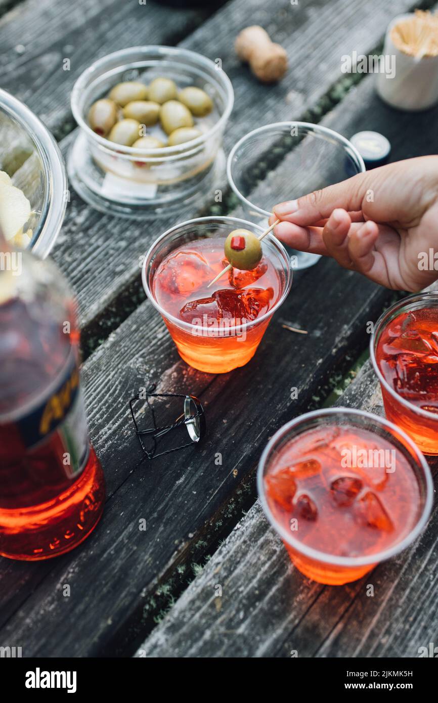 Donna mettere l'oliva verde in Aperol spritz frizzante aperitivo cocktail all'aperto sul tavolo da picnic Foto Stock