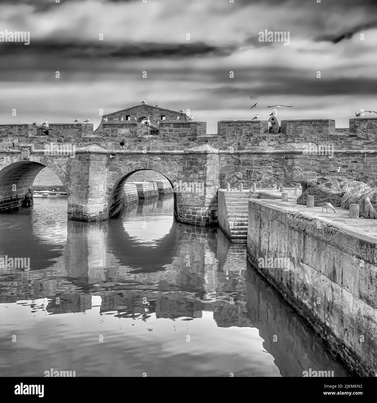 Un'immagine in scala di grigi di un vecchio ponte merlato su un fiume in Marocco con canoni a sinistra dal Medioevo Foto Stock