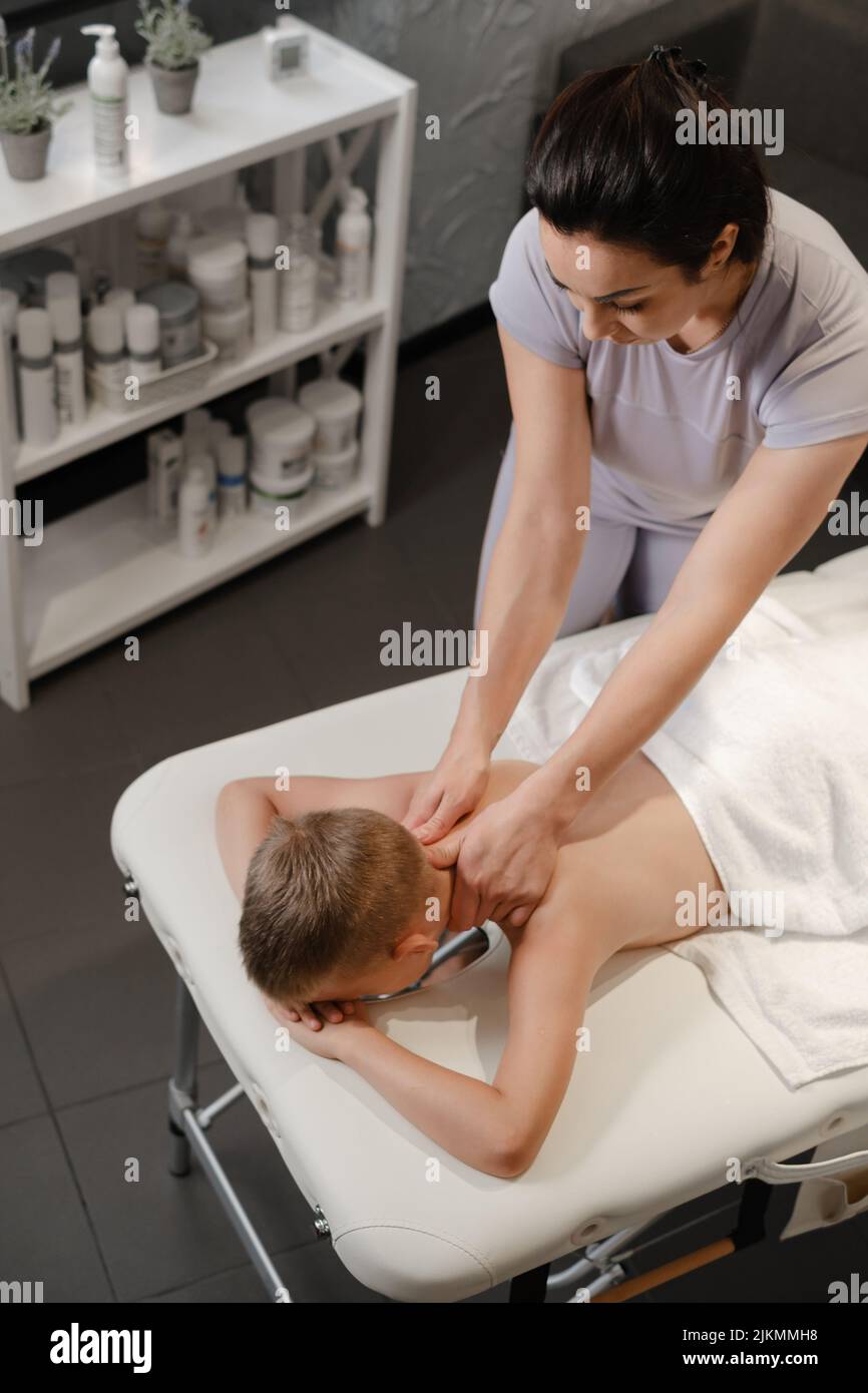 il massaggiatore dona al bambino un massaggio alla schiena. Massaggio bambini. Massaggio terapista con massaggio spalle di 7 anni. Terapia fisica Foto Stock