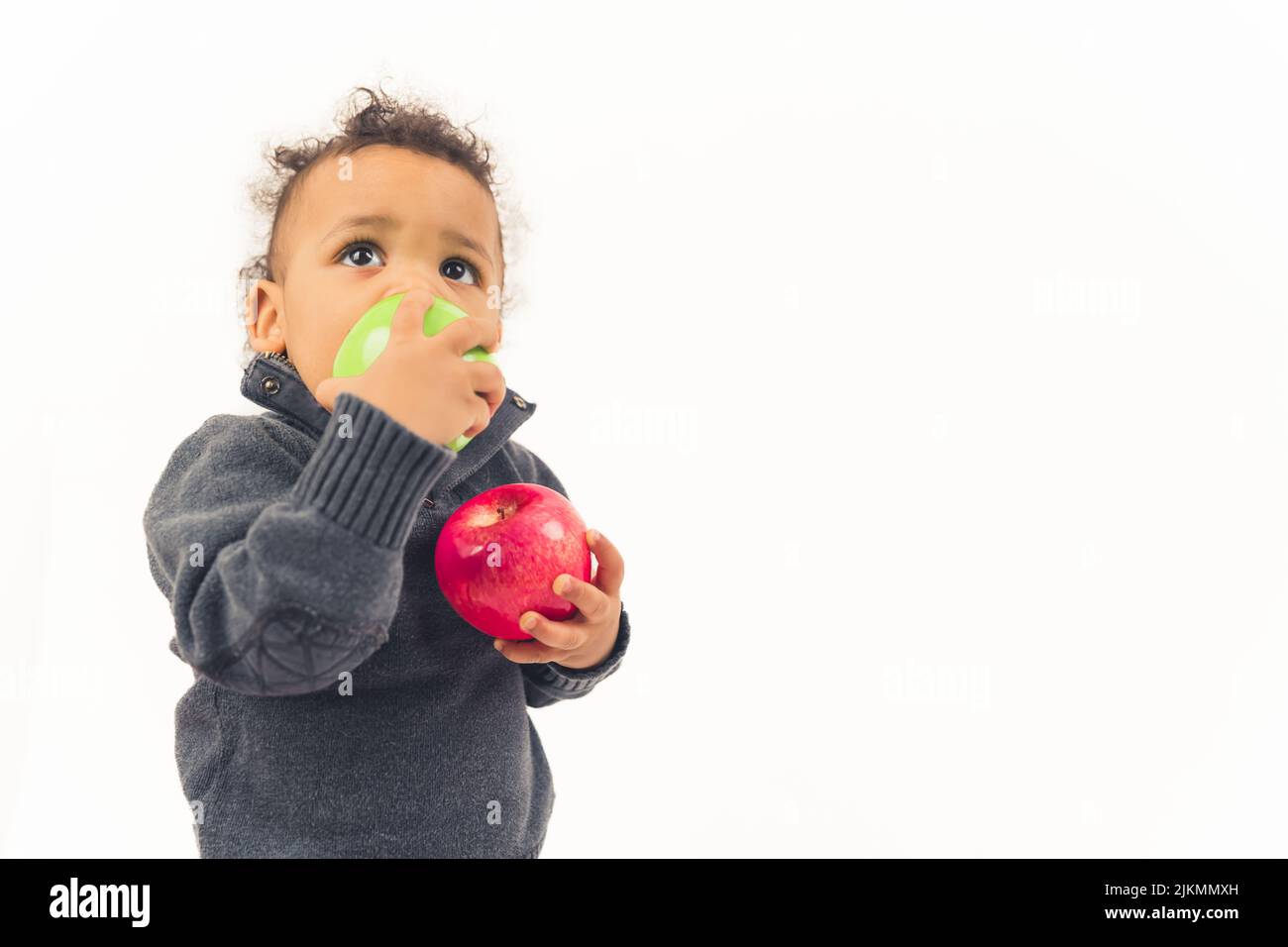 Piccolo afroamericano maschio ragazzo mangiare una mela con la mano destra e tenere un'altra mela con un'altra - closeup isolato. Foto di alta qualità Foto Stock