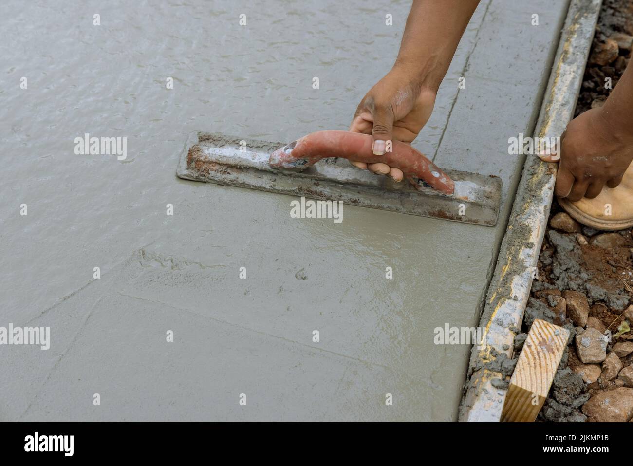 Un lavoratore sta lavorando su un nuovo marciapiede che è stato appena versato su calcestruzzo bagnato mentre tiene una cazzuola d'acciaio Foto Stock