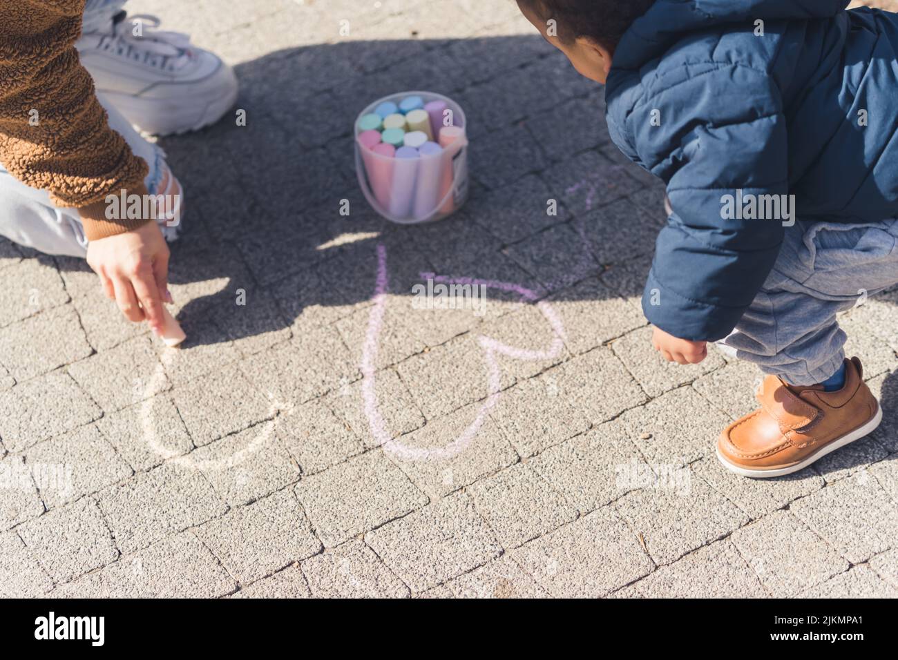 Un piccolo ragazzo africano di 5 anni e sua madre che disegnano ascolta sul marciapiede usando pastelli colorati. Foto di alta qualità Foto Stock