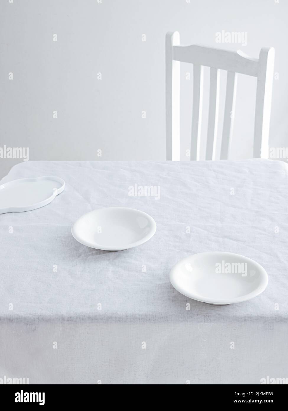 Un tavolo con piatti e una sedia in un ambiente minimalistico bianco Foto Stock