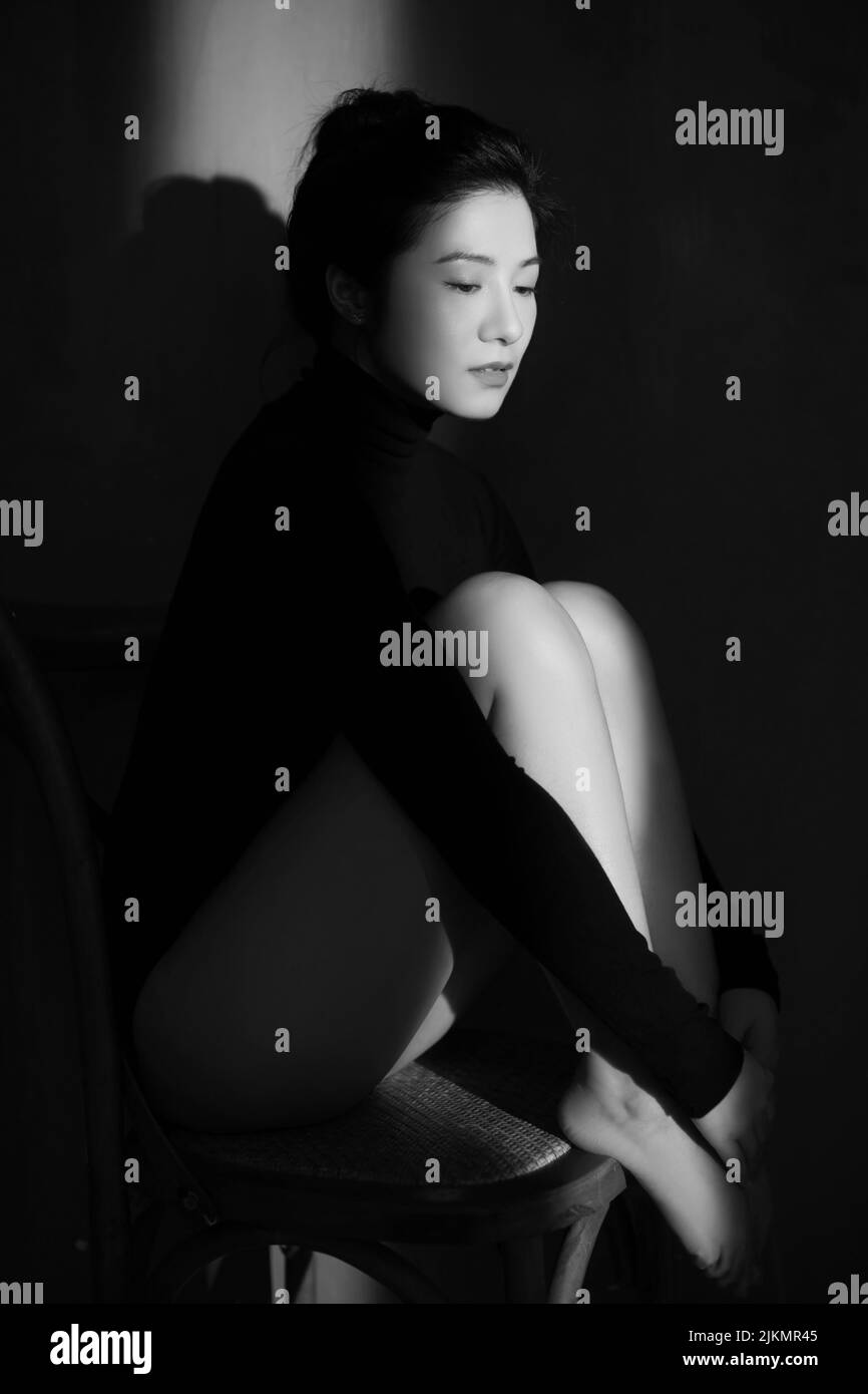 Una foto verticale di una donna dell'Asia orientale seduta sulla sedia di legno Foto Stock