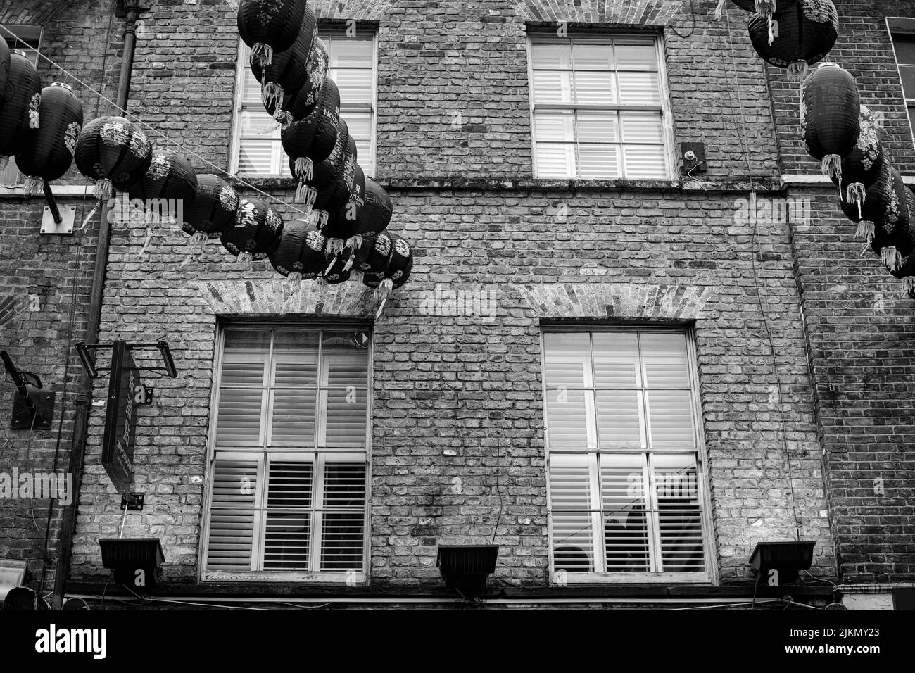 Un basso angolo in scala di grigi dell'edificio di China Town con Lanterne e carte appese decorate, Londra, Regno Unito Foto Stock
