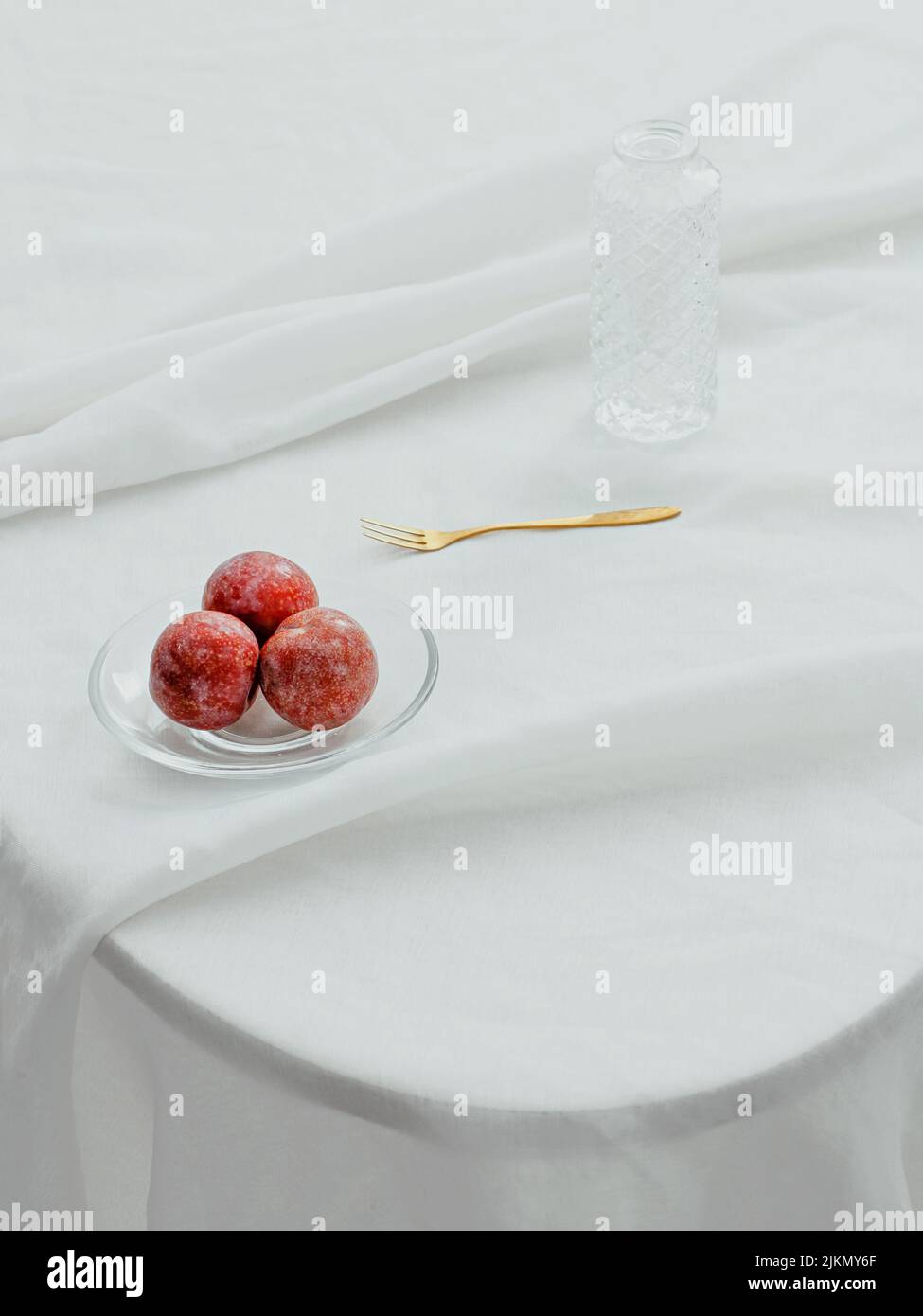Un colpo estetico verticale di mele su un piatto trasparente, una forchetta e una bottiglia di vetro su un tavolo con copertura in tessuto bianco Foto Stock