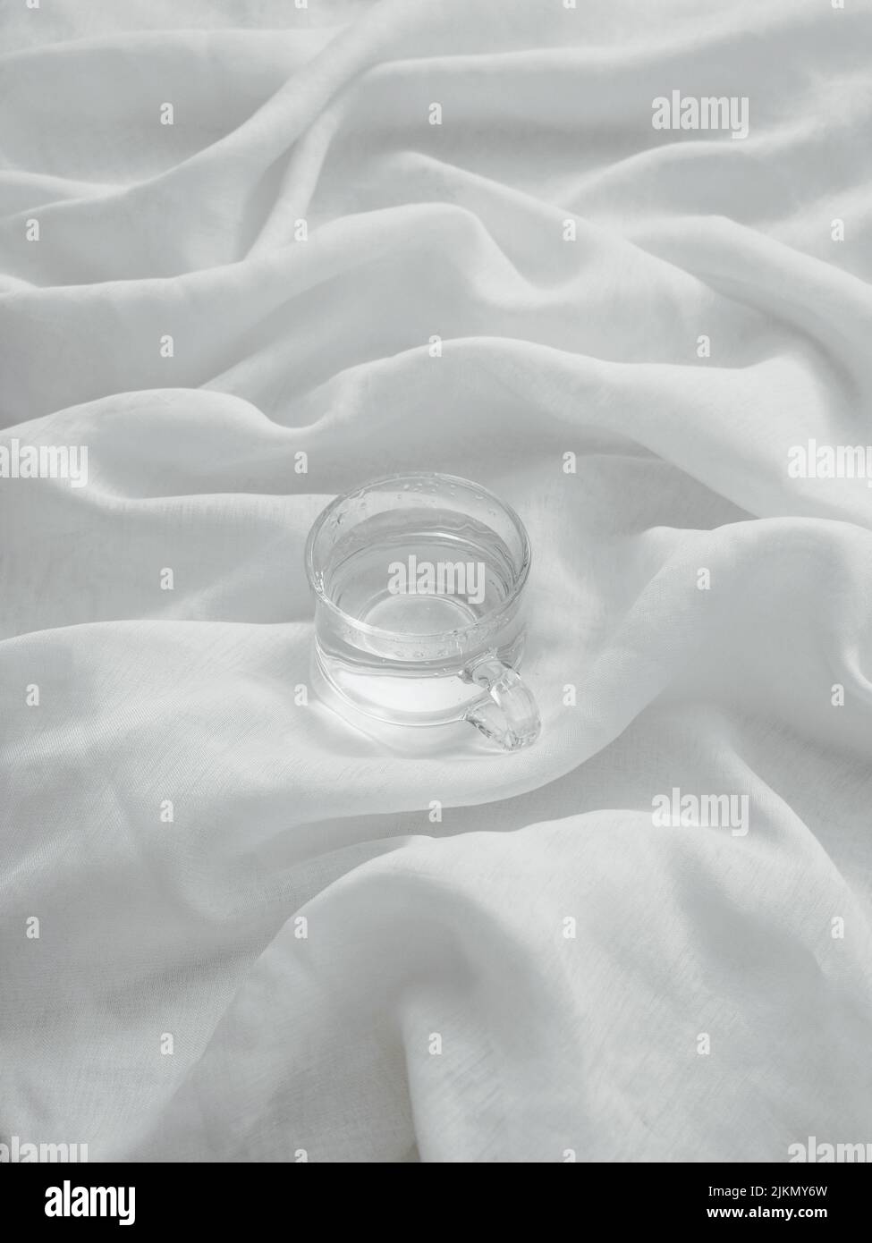 Un colpo estetico verticale di un bicchiere d'acqua su una superficie di tessuto Foto Stock