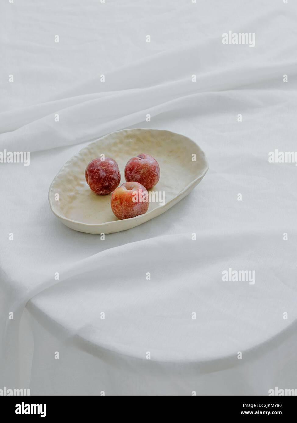 Un colpo estetico verticale di mele in una ciotola bianca su un tavolo con copertura in tessuto bianco Foto Stock