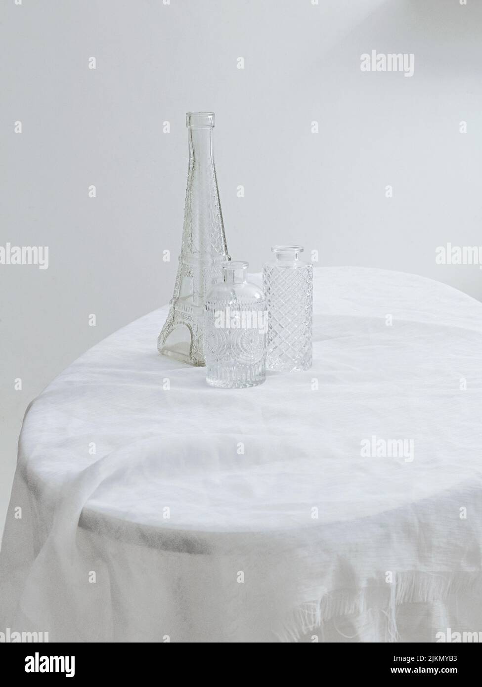 Una foto estetica verticale di tre diverse bottiglie di vetro su un tavolo ricoperto di tessuto bianco Foto Stock